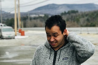 A man in a grey sweater standing in the middle of a road.