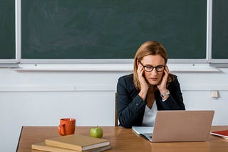 Teacher working at computer, head in hands.