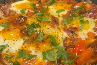 Delicious protein in my homemade shakshuka. Sunnyside eggs on bed of onions tomatoes, spices, and garnished with fresh cilantro