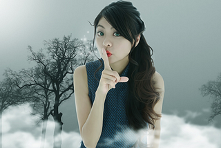 Asian woman holding her finger to hush. Clouds and trees in background.