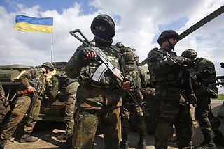 Infantry gather for an operation, 4 soldiers stand with a Ukrainian flag in the backround. They have forest camo and AK 47s.