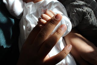 Newborn baby holding her mother’s finger