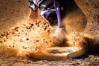 A baseball player sliding into a base with dirt everywhere.