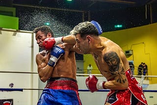 Two men fighting in a boxing ring with one wearing a red shirt.
