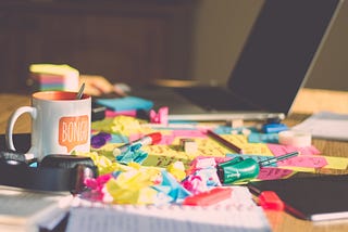 A messy desk with lots of colourful post it notes, a laptop and a mug. (Not my desk) Photo: Ferenc Horvath on Unsplash