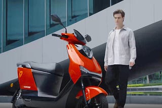 A red Yadea Ezeego electric scooter being approached by a rider in front of a city building.