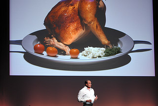 on a dramatically lit stage, full body shot, a person reveals a new roast chicken dish, dramatic presentation”