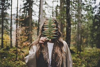 Woman standing in the woods holding a fern leave in front of their face