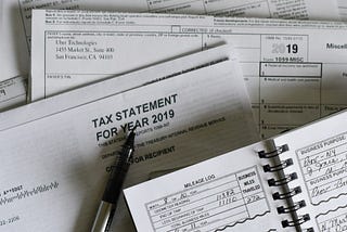 Tax documents and 1099 forms with a tax statement, pen and business log on a desk during tax season. Photo by Olga DeLawrence on Unsplash