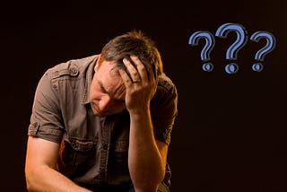 Man slumped forward, head in his left hand, with three question marks alongside him.