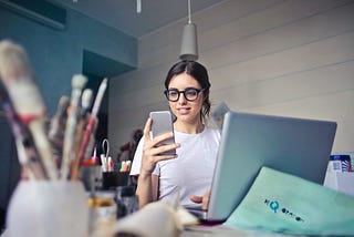 A lady working at a cluttered desk, reading on her phone