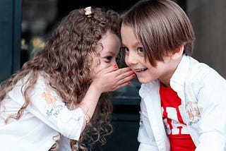 Two children, girl and boy around five years old with obvious joy, are whispering secrets.