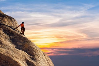 A woman rockclimbing up a cliff with the sunset in the background.