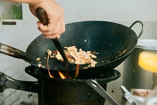A person cooking food in a wok on a stove.