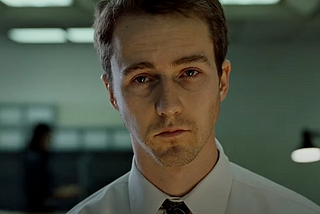 Close-up of the unnamed narrator from the film “Fight Club” (1999), portrayed by Edward Norton, looking tired and disillusioned under harsh office lighting.
