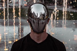 Man with mirrored mask in front of a fountain.