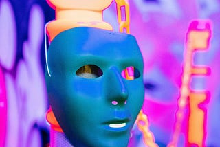 A full face mask hanging from a neon stanchion in front of a vibrant and blacklit, out of focus party entrance.