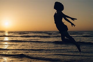 silhouette of someone jumping in the air with the ocean and sunset in the background