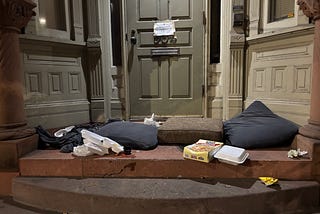 A doorway with food packaging and cushions for sleeping