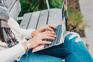 Woman sitting on bench outside typing on laptop