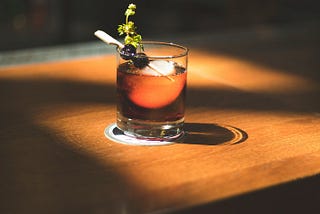a glass with brown liquor garnished with cherries and a sprig of an herb