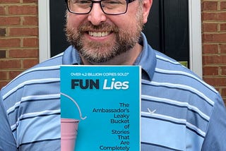 Picture of Mark Suroviec, M.Ed., holding his new book “FUN Lies: The Ambassador’s Leaky Bucket of Stories That Are Completely Half True.”