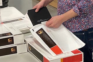 A T-Mobile staff person places a box containing a tablet into a plastic shipping sleeve.