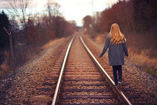 Photo of a girl walking down an empty railway track at sunset