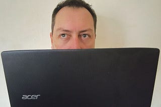 man sitting with laptop peering over the top with annoyed expression