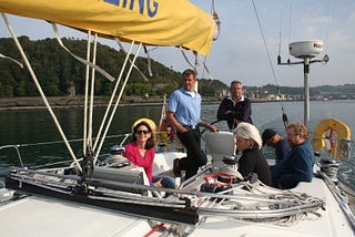 Six crew-members on the deck of a forty-six foot Bavaria yacht leaving Oban harbor