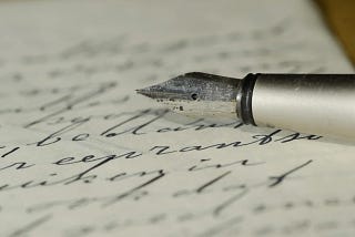 Stock photo of a white paper filled with words in cursive writing using an ink pen with one third of the pen lying on the paper
