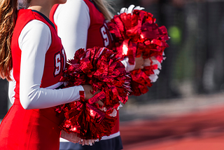 Close up photo of two cheerleaders dressed in red holding red and white pom-poms.