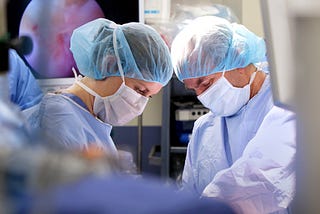 Resident and attending physician performing an orthopedic surgical procedure in a hospital operating room.