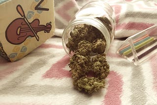 Mason jar of cannabis flower surrounded by baby toys laid on a baby blanket.