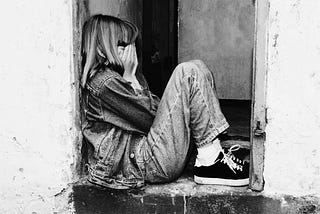 Lonely girl sitting on a doorway, face buried in her palms