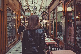 Backside of a woman in leather jacket walking through a shopping center.