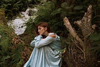 Woman in blue dress sitting on tree trunk lost in deep thoughts