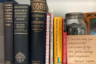 A photo of some English grammar and and usage guides, including some hardbacks (e.g., “Fowler’s Modern English Usage” and a dictionary of classical quotations) and softbacks (e.g., Strunk and White’s “The Elements of Style”). A quote in handwritten calligraphy on a small card sits to the right: “There are only four subjects in the curriculum of life — love, justice, courage, and compassion. — Richard Trelease.” (Photo by author.)