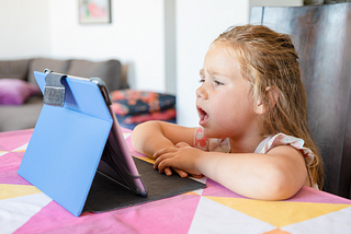 A young girl sitting at a counter, talking into an iPad.