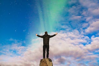 A man stands on top of a rock with arms outstretched towards the sky.