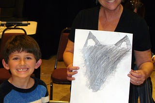 Artist and student smile broadly as a wolf drawing is completed.