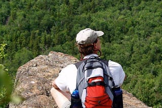 W Michael Donovan sits cross-legged on a rock outcropping while on a hike and stares out at the forest below.