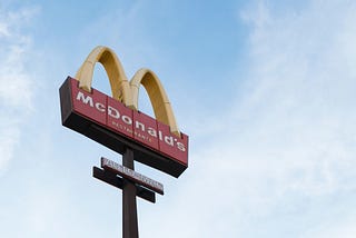 A yellow M letter of McDonald’s logo seen from below with sky as background