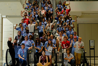 About 40 to 50 DSA members a part of the MUG caucus stand on a set of three elevators, some with fists raised.