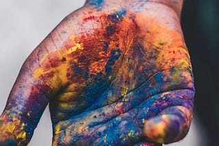 Human right hand covered in many brightly coloured paints.