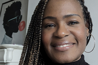 A lady with braids in front of a graphic picture of a man blowing a bubble