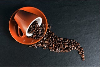 A rustic orange saucer and coffee mug. The mug is flipped over with coffee beans pouring out: Spilling the beans.