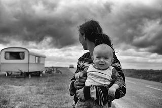 Baby looking at the camera while woman holding it looks behind her toward a trailer.