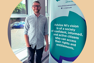 Alsdair from Advice NI standing next to a pop-up banner of Advice NI