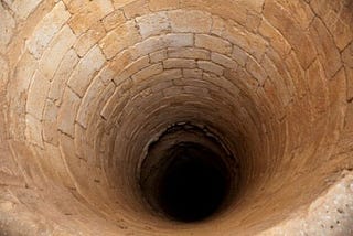 A bottomless pit lined with taupe sandstone brick